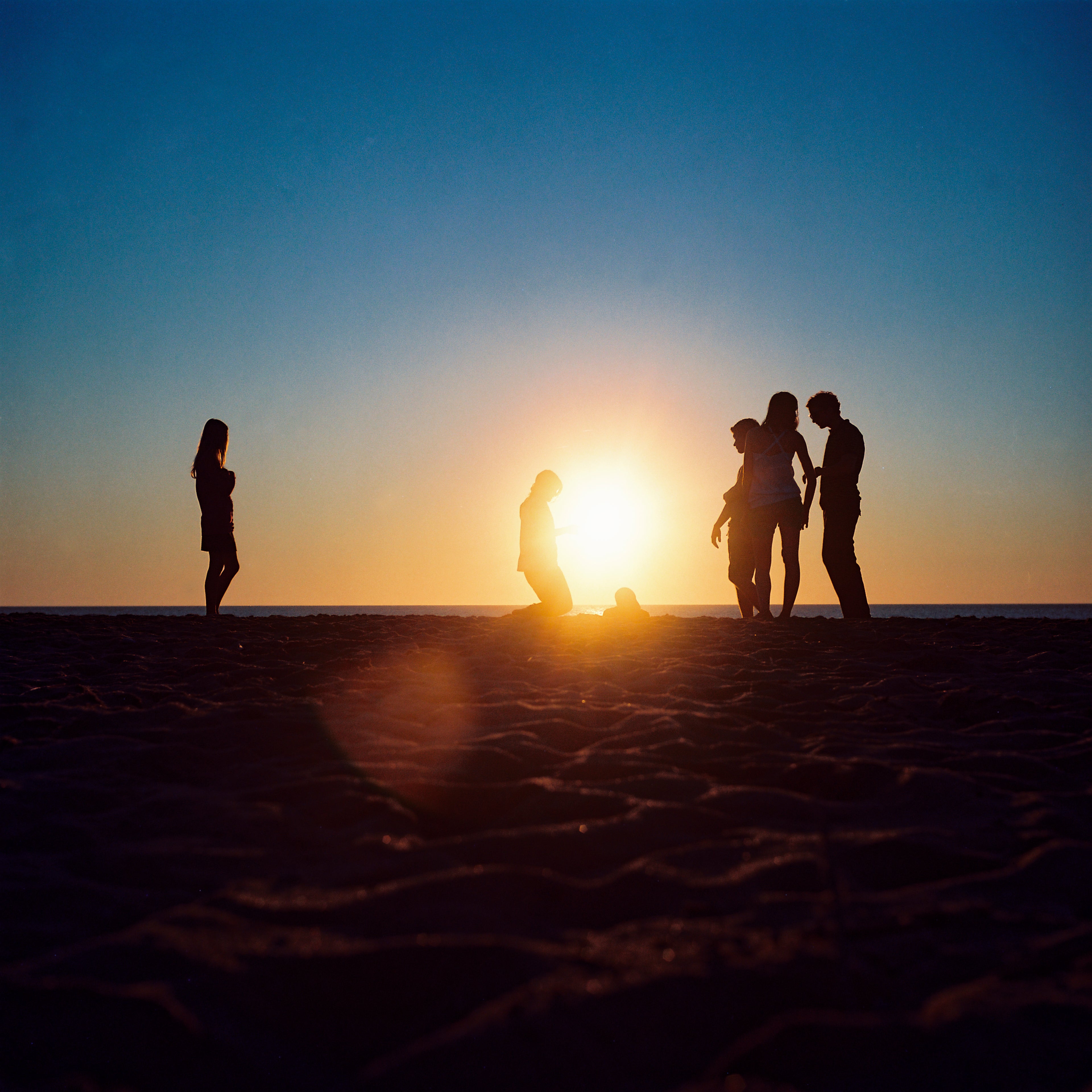 Silhouettes of people on a beach with the sun over the sea.